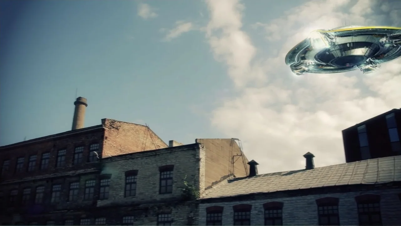 UFO Conspiracies: The Hidden Truth (2020) movie still: wide — A view of old brick industrial buildings under a cloudy daytime sky. A metallic,…