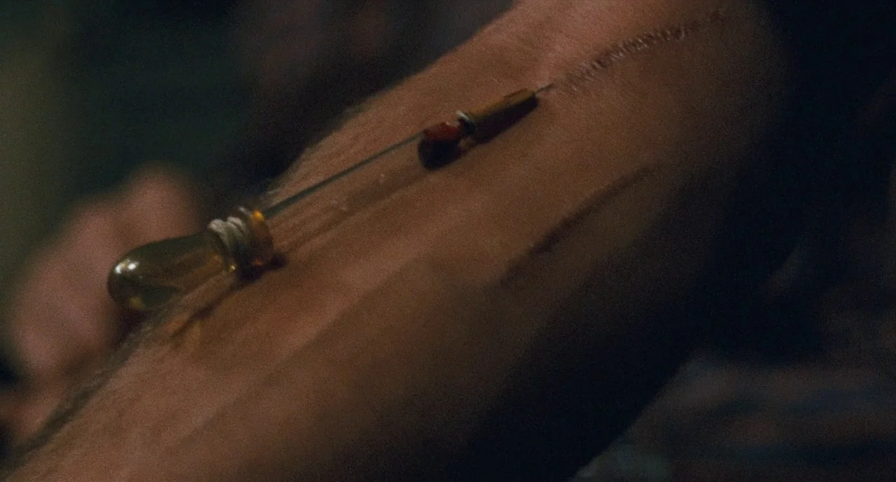 The Panic in Needle Park (1971) movie still: closeup — A close view of a glass dropper laying horizontally across dark skin. The glass surface…