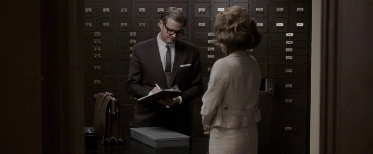 A Single Man (2009) movie still: medium — A high-security bank vault is lined with hundreds of metal safe deposit boxes. A man in a suit consults a…