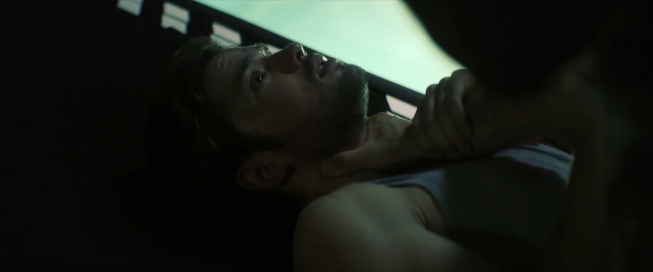 Tell Me How I Die (2016) movie still: closeup — A dark vehicle interior with a structural frame visible above the subject's head. A man lies on his…