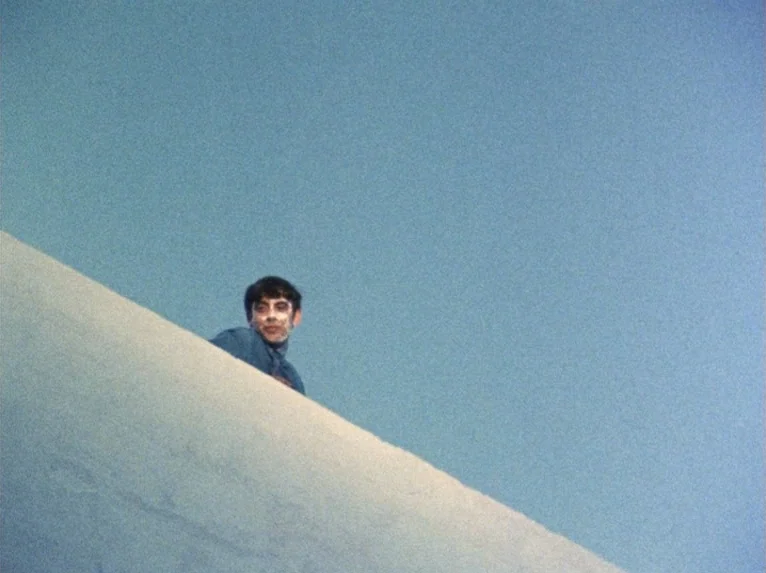 Our Lady of the Turks (1968) movie still: wide — A man looks over the edge of a white curved concrete structure against blue sky. The clear blue sky…