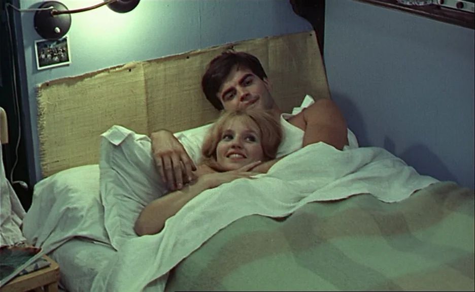 Le Bonheur (Happiness) (1965) movie still: medium — A man and a woman rest together in a small bed with blue walls. The couple lies beneath white…