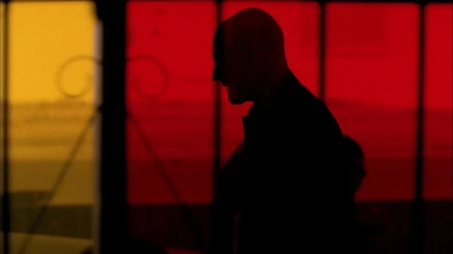Breaking Bad (2008) movie still: medium — A man stands before a wall of red and orange tinted glass panels. The subject is backlit, appearing as a…