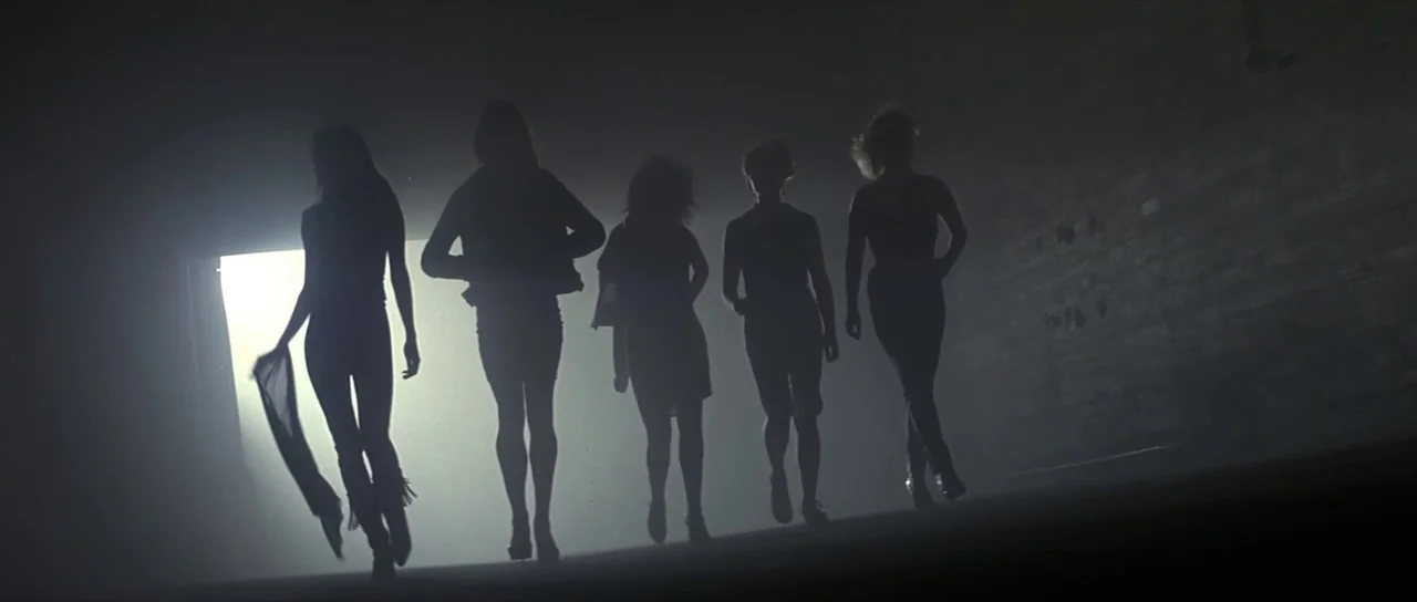 Pink Floyd The Wall (1982) movie still: fullbody — A dark, textured tunnel with a bright light source at the far end. Five women walk forward in a…