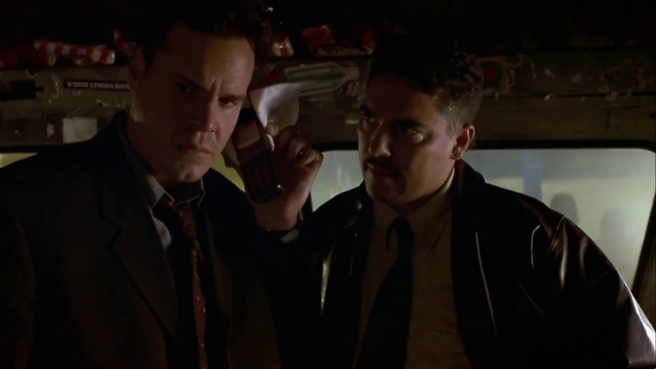 Hellraiser: Inferno (2000) movie still: medium — Two men sit inside a vehicle at night under dark, shadowed lighting conditions. One man holds a…