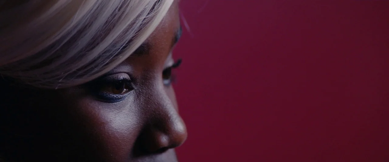 Girlhood (2014) movie still: closeup — A close-up view of a woman's face against a solid dark red background. She gazes slightly off-screen with…