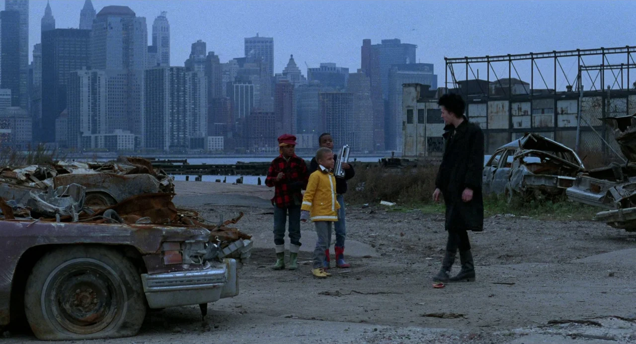 Sid and Nancy (1986) movie still: wide — A derelict waterfront lot filled with rusted, stripped car husks and grey dirt. Three young children watch…