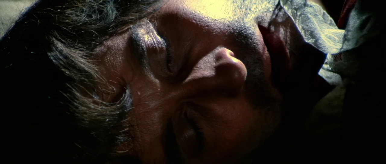 Night of the Blood Monster (1970) movie still: closeup — A close-up view of a person lying down in a dark room. The man rests with eyes closed while…
