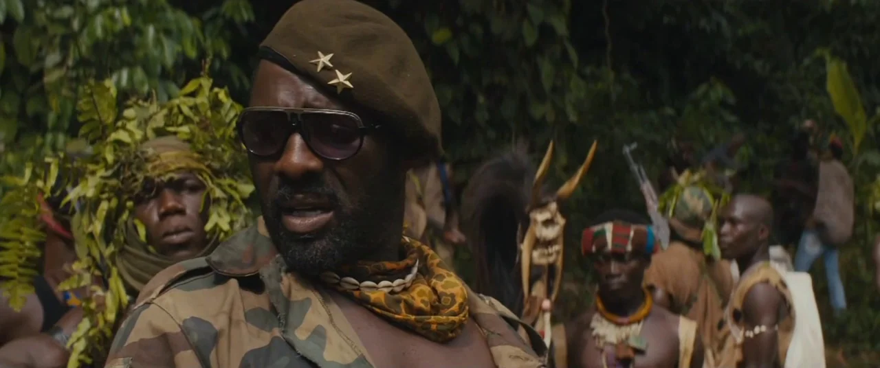 Beasts of No Nation (2015) movie still: medium — A dense green tropical jungle serves as a background for a small militia group. A man in a beret…