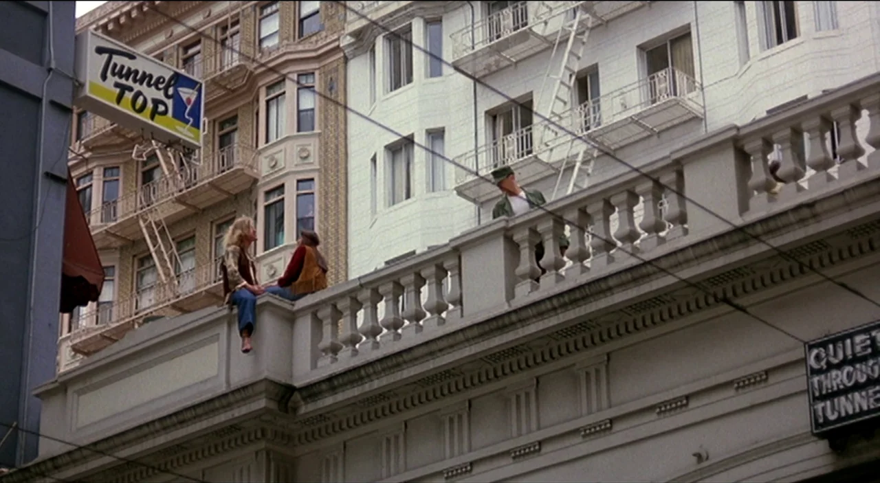 Dogfight (1991) movie still: wide — A historic building facade features a stone balustrade and white painted exterior walls. Three individuals sit…