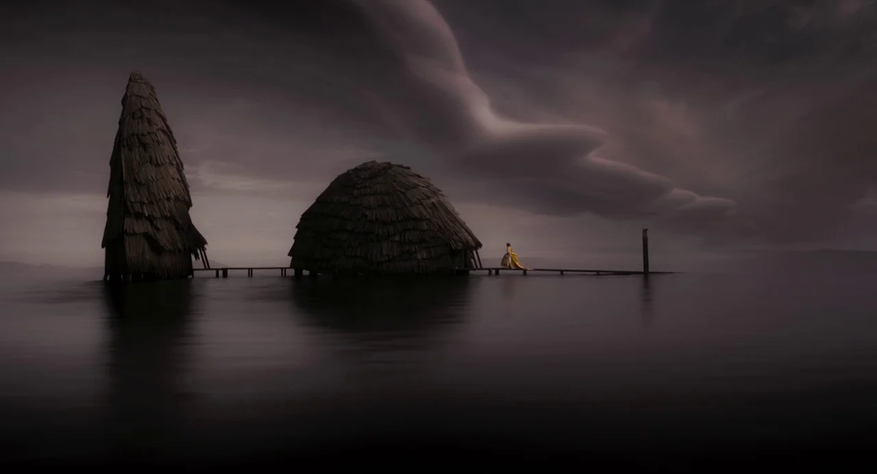 Mirror Mirror (2012) movie still: wide — Two large wooden stilt structures connected by a narrow pier rise from dark water. A lone woman in a bright…