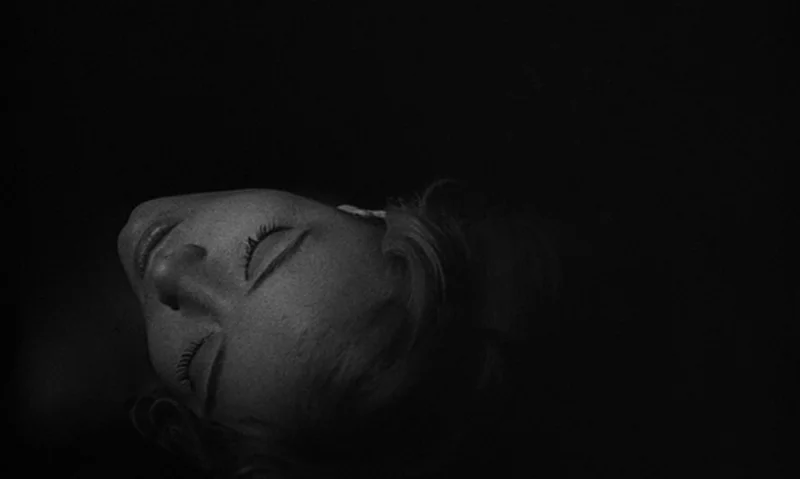Man Is Not Bird (1965) movie still: closeup — A woman's face is partially lit in an otherwise pitch-black, featureless space. Her head is tilted…