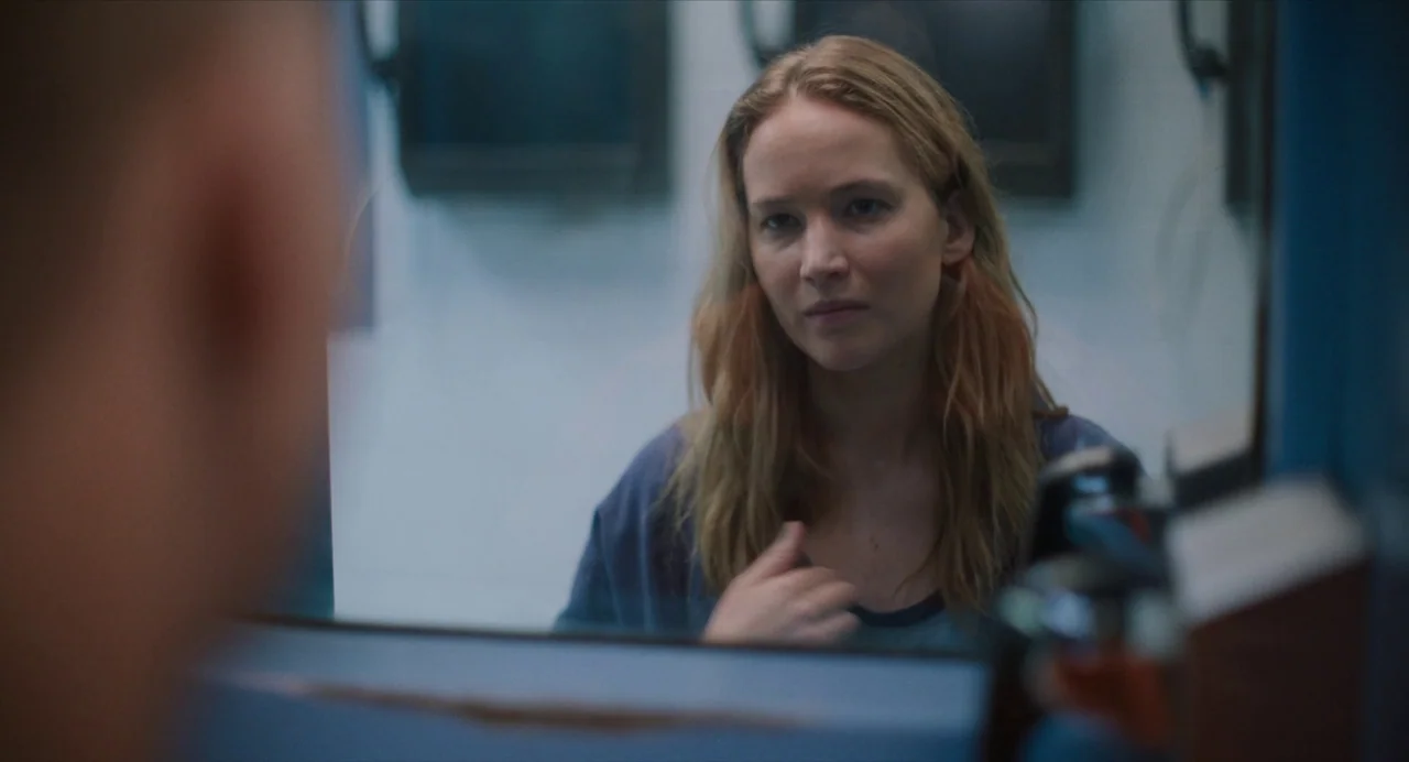 Causeway movie still: medium — A dimly lit room with plain walls and a mirror frame. A woman stares into the glass while observing her own reflection.