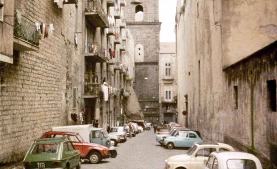 The Kingdom of Naples (1978) movie still: establishing — A narrow residential street in a city is lined with tall stone buildings. Several small…