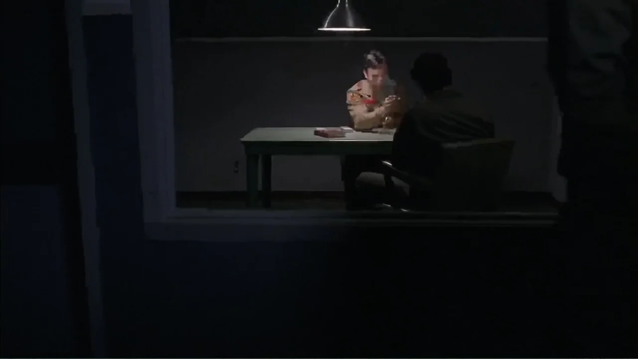 Day of the Dead 2: Contagium (2005) movie still: wide — A dimly lit, sparse interrogation room features a single metal table under one light. Two…