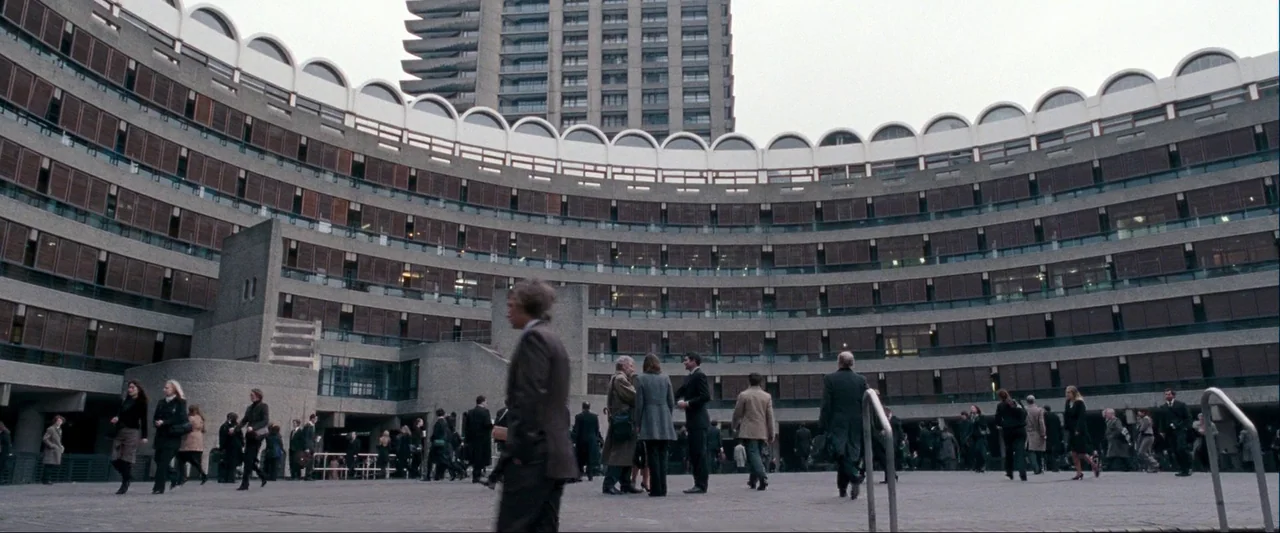 Quantum of Solace (2008) movie still: wide — A massive Brutalist concrete complex with curved balconies surrounds a paved open courtyard plaza.…
