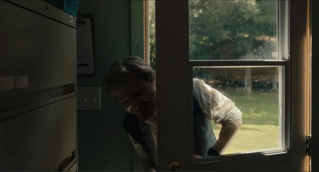 Hell of a Summer (2025) movie still: medium — An interior office space with a metal filing cabinet stands near an open door. A man leans through the…