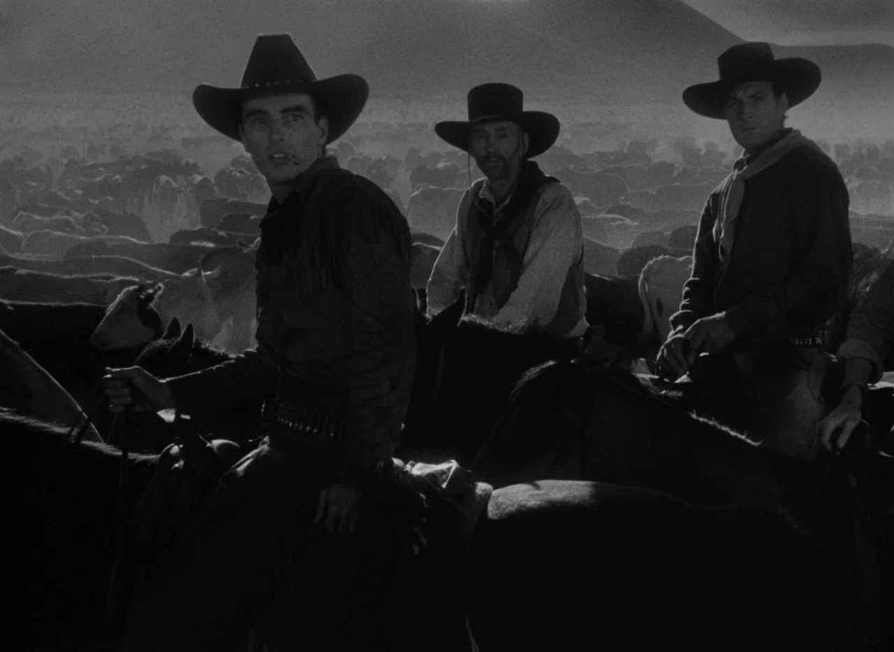 Red River (1948) movie still: medium — A vast, dusty open range filled with a large herd of grazing cattle. Three cowboys sit on horseback in the…