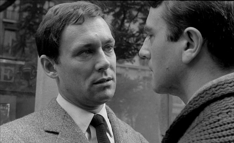 Le Feu Follet (1963) movie still: medium — Two men stand closely together on a city sidewalk during the day. They are engaged in a tense…