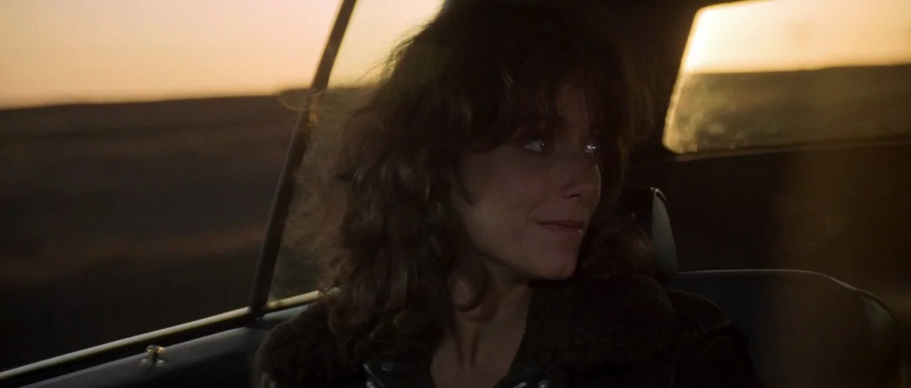 Starman (1984) movie still: closeup — Inside a vehicle looking out across an expansive, desolate landscape during golden hour. A woman sits in the…