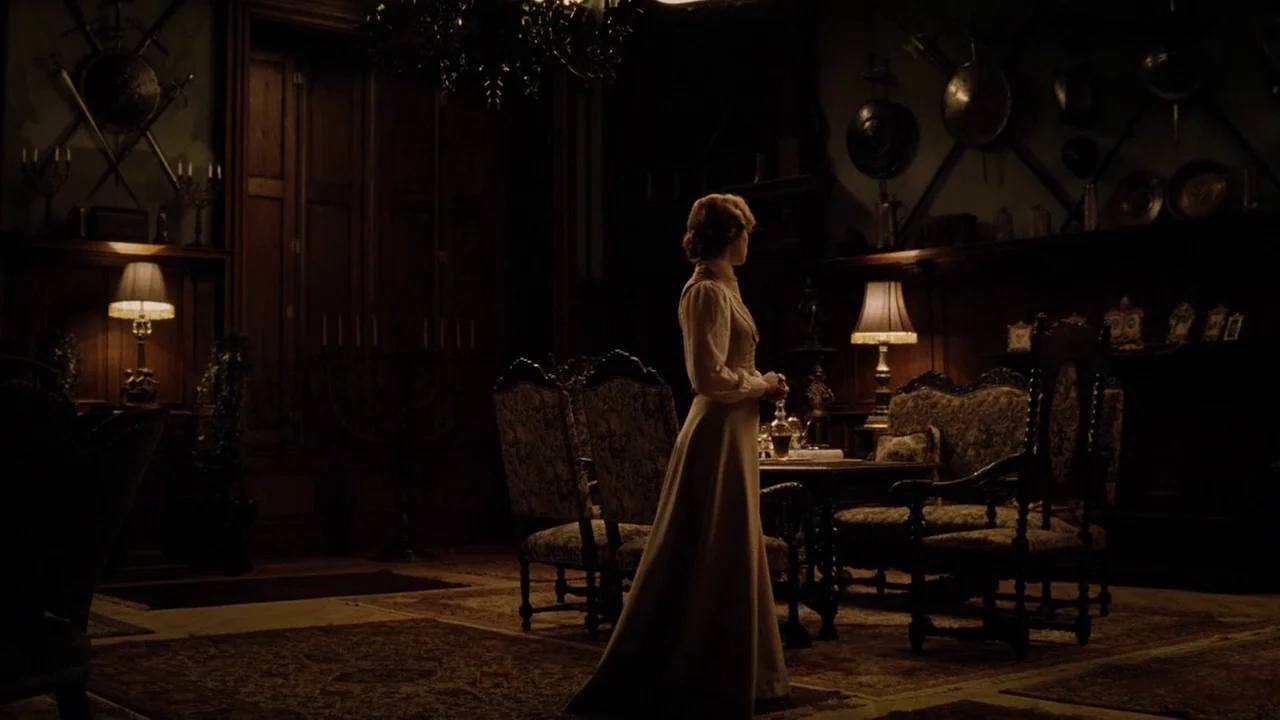 The Illusionist (2006) movie still: fullbody — A dark, wood-paneled room features antique furniture and walls adorned with shields and swords. A…