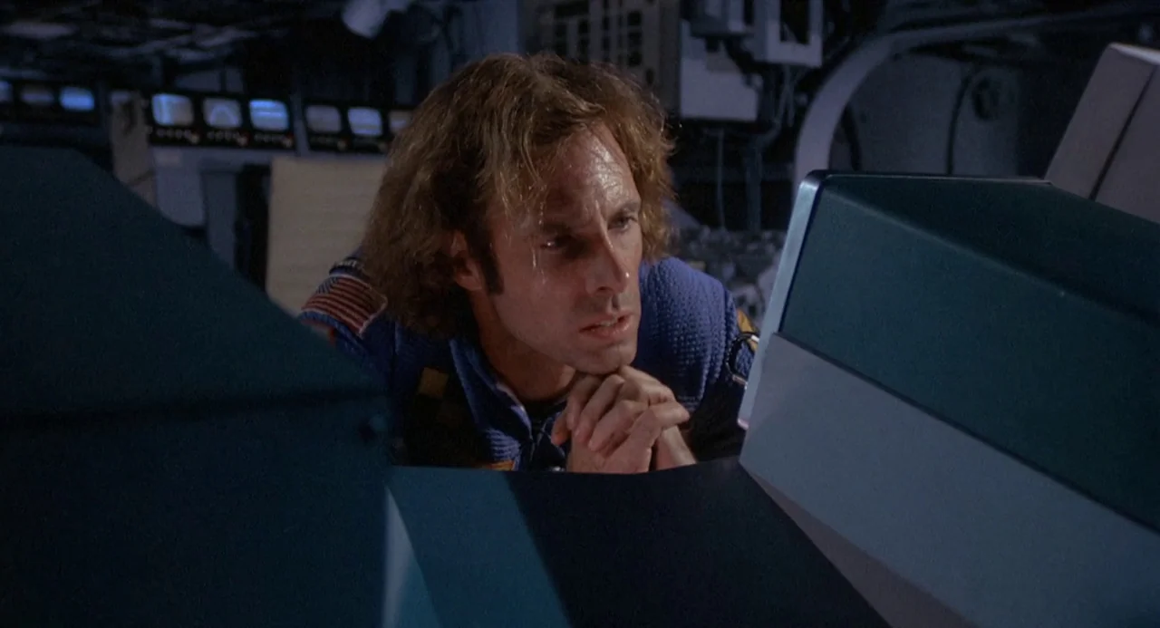 Silent Running (1972) movie still: medium — A dimly lit spacecraft control station with rows of small glowing status monitors. A man in a blue…