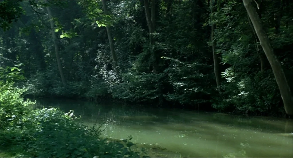 On War (2008) movie still: establishing — A quiet river flows through a dense, lush green forest with overhanging branches. Tall trees line the…