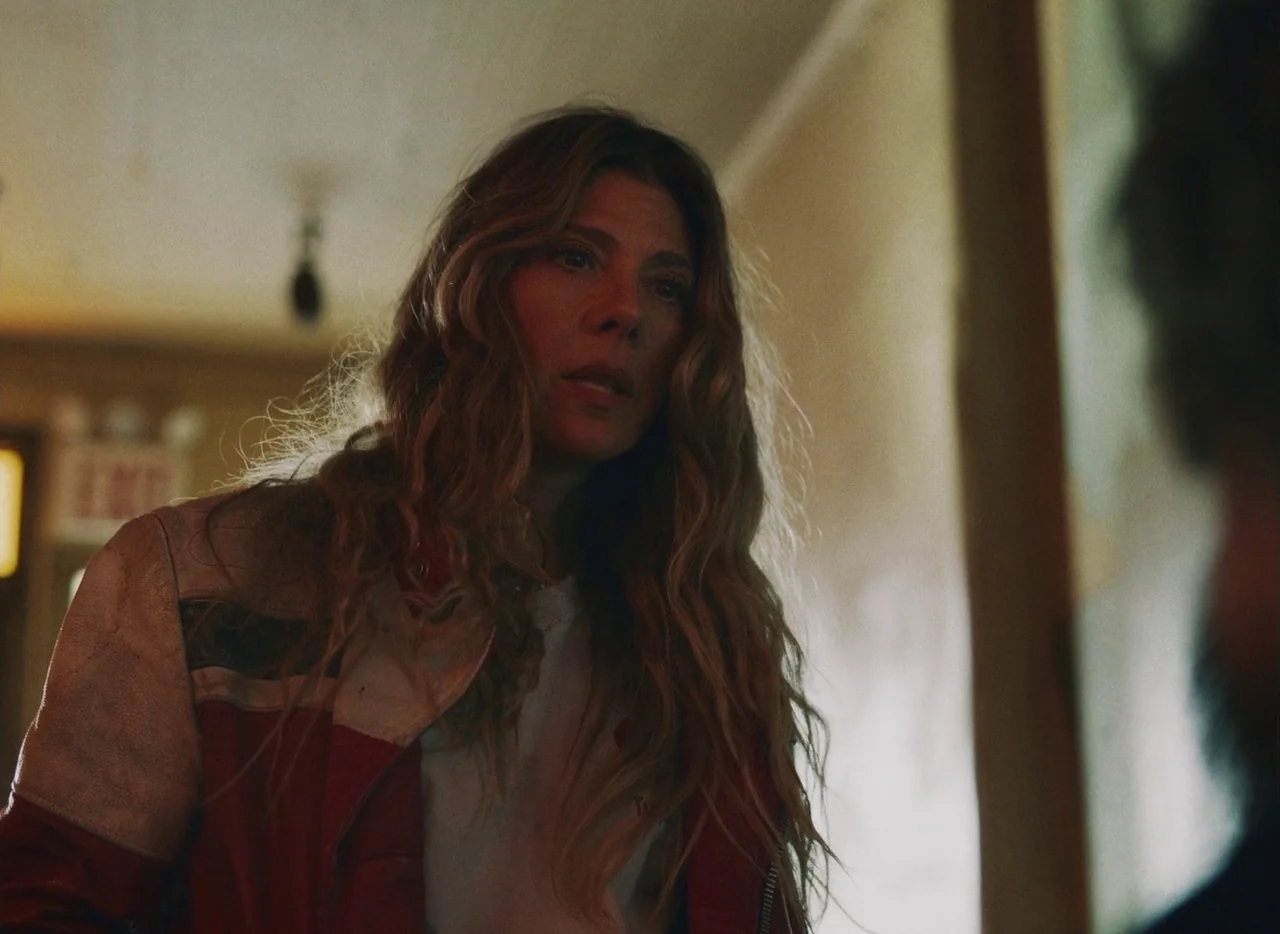She Came To Me (2023) movie still: medium — A dimly lit interior hallway with visible walls and an exit sign in distance. A middle-aged woman stands…