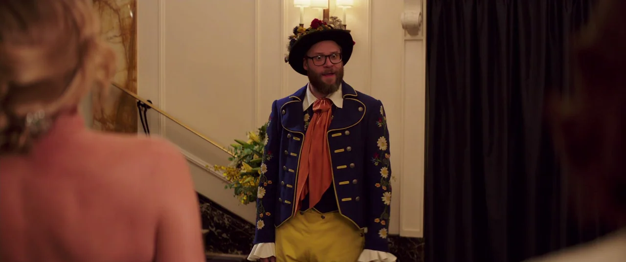 Long Shot (2019) movie still: medium — An upscale foyer features ornate wall paneling and a dark curtain on the right. A man dressed in a stylized,…