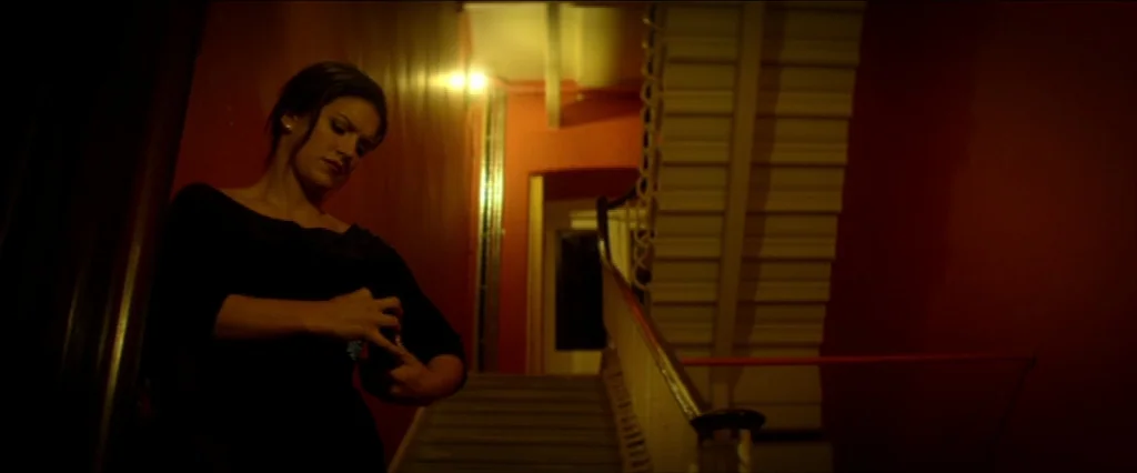 Haywire (2011) movie still: medium — An interior staircase features vibrant red walls and a white-railed staircase illuminated by warm lighting. A…