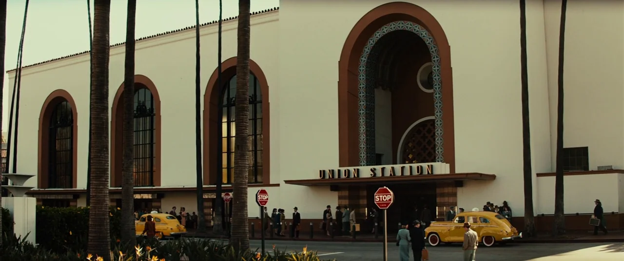 Gangster Squad (2013) movie still: wide — A large Mission Revival style terminal building has tall arched windows and palm trees. Multiple people in…