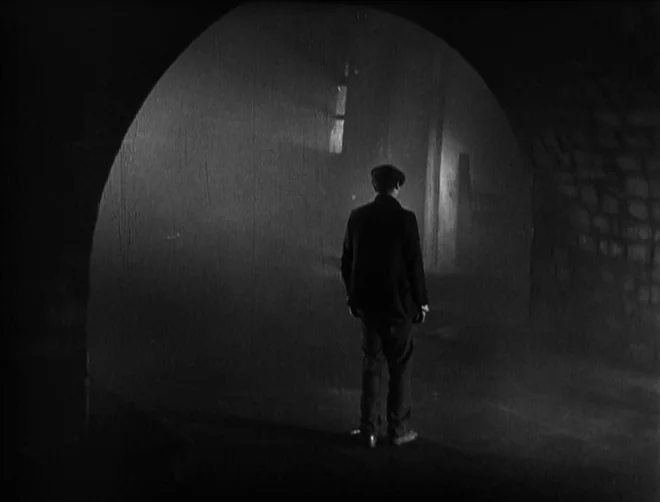 Pandora’s Box (1929) movie still: fullbody — A dark stone tunnel is illuminated by distant light at the end. A lone man in a suit stands facing away…