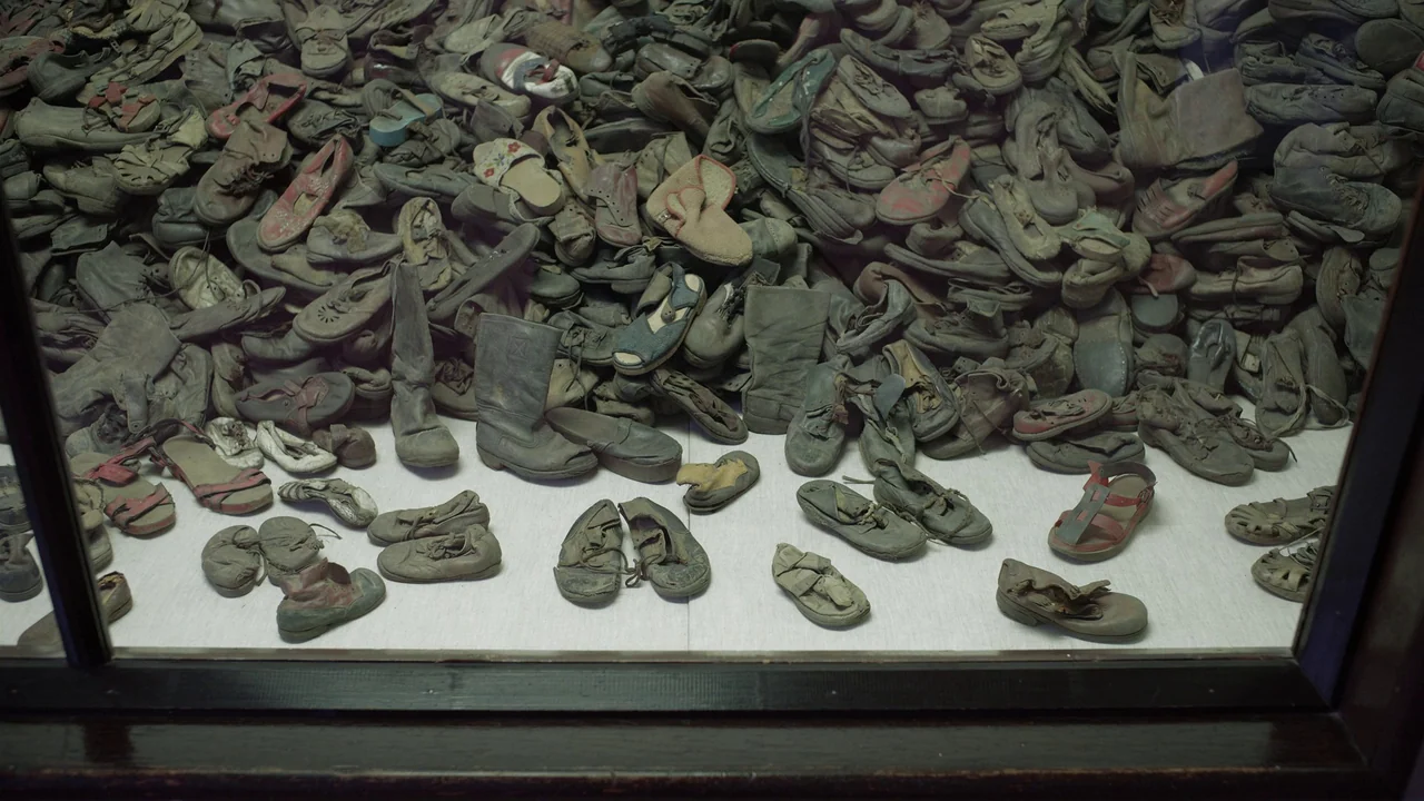 The Zone Of Interest (2023) movie still: wide — A glass-enclosed display case contains a massive, dense mound of weathered, discarded shoes. The…