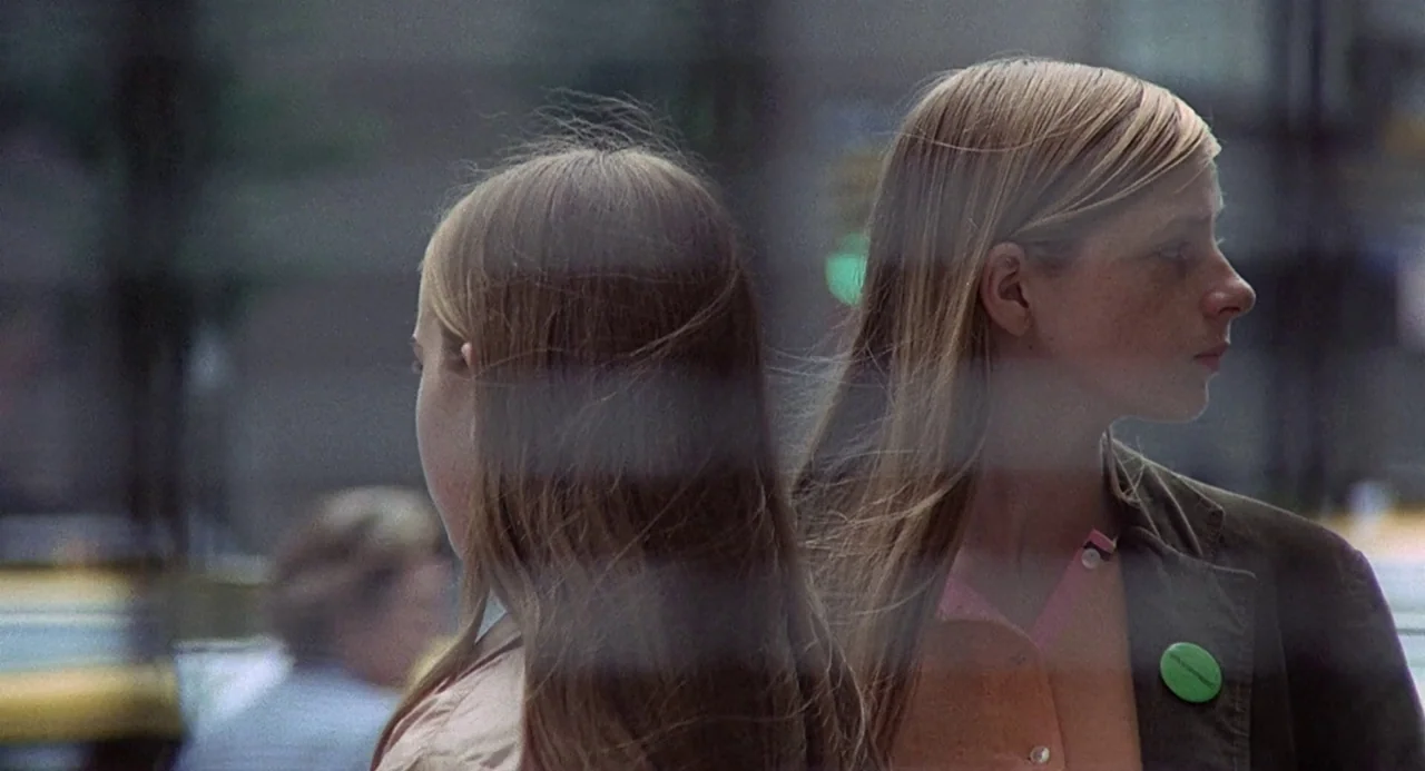 Taking Off (1971) movie still: medium — A city street scene viewed through a glass window with reflections of traffic. Two blonde teenage girls…