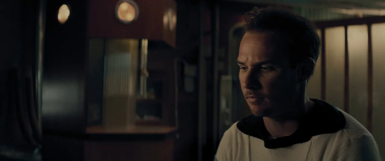 Domain (2017) movie still: medium — A dark train carriage with illuminated circular lamps visible against the rear wall. A man sits in the…