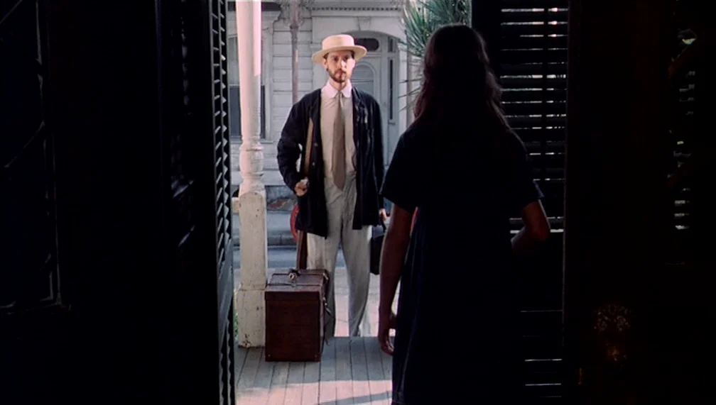Pretty Baby (1978) movie still: fullbody — A man holding a suitcase stands on a residential porch facing a doorway. A woman stands in the doorway…