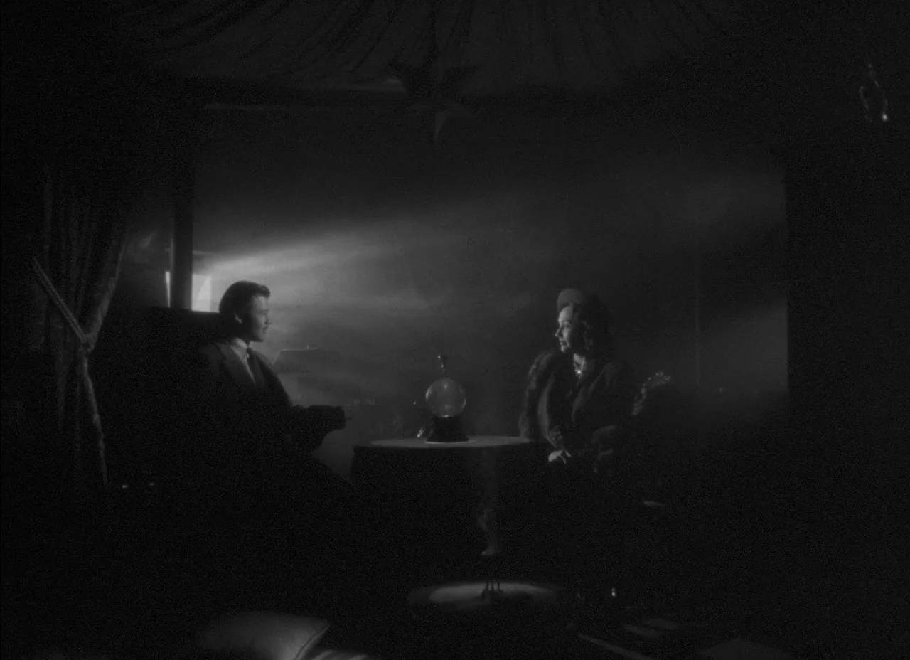The Amazing Mr. X (1948) movie still: wide — A dimly lit room features a small round table situated between two seated figures. A focused beam of…