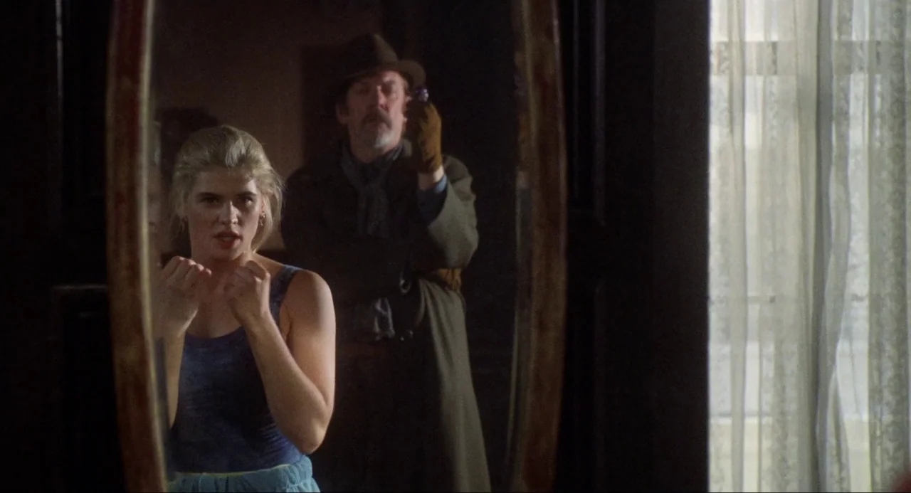 Buffy the Vampire Slayer (1992) movie still: medium — A dimly lit room features a large oval mirror reflecting a woman and man. The woman mimics a…