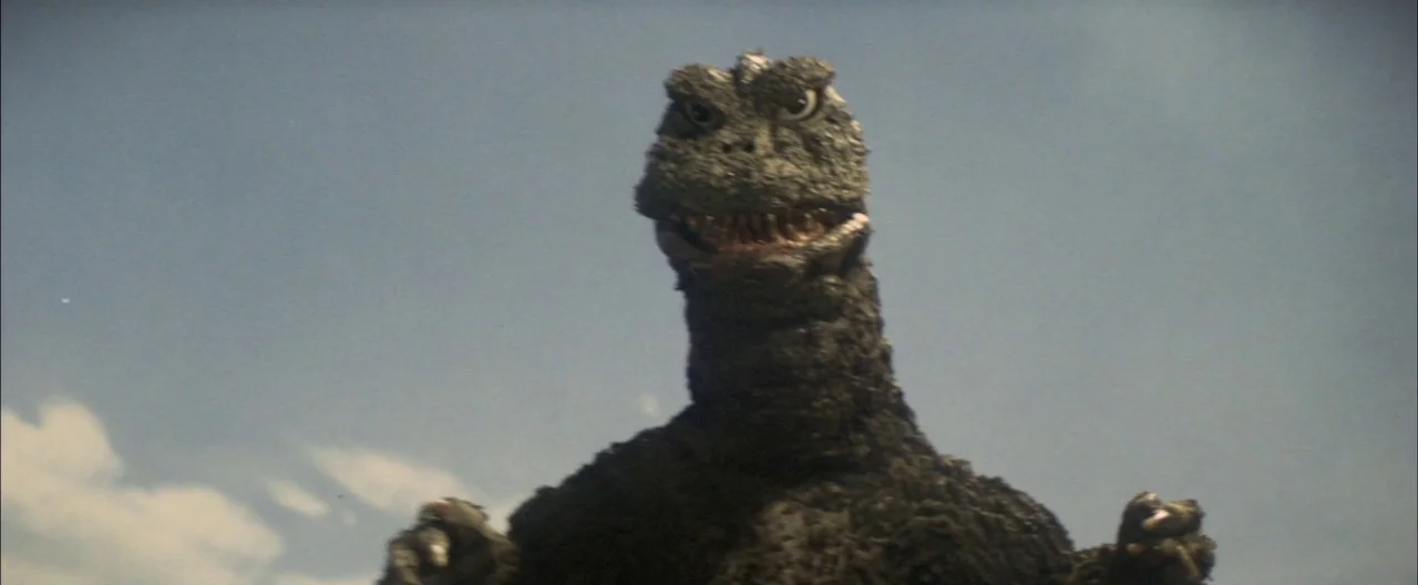 Destroy All Monsters (1968) movie still: medium — A giant reptilian creature stands against a clear daylight sky with minimal clouds. The subject is…