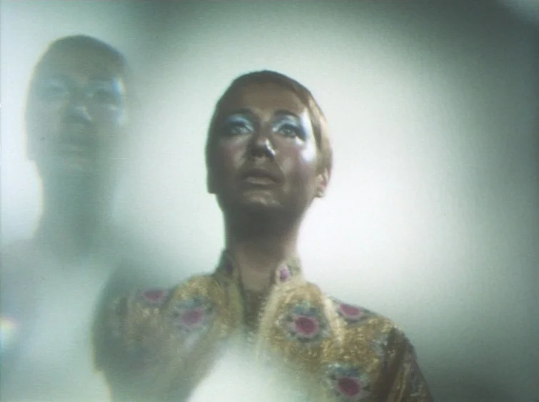 Hermitage (1968) movie still: medium — Two individuals stand in a hazy, white-lit interior setting with blurred focus. The foreground person wears a…
