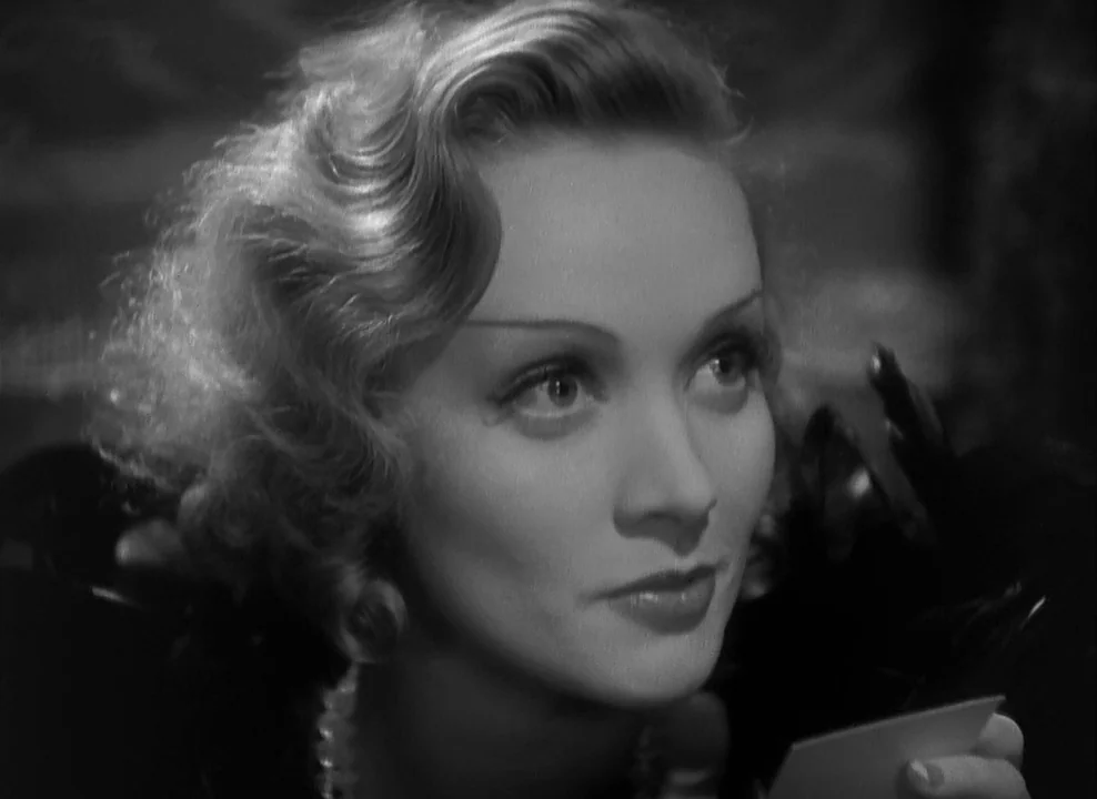Shanghai Express (1932) movie still: closeup — A dark, dimly lit indoor space with feathered textures visible in the foreground. A woman looks…