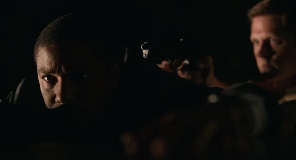 Just Mercy (2019) movie still: medium — Two men are positioned in a dark, undifferentiated environment holding firearms. They watch ahead with…