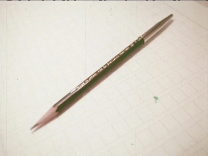 Catalogue of Memory (1977) movie still: closeup — A dark green drafting pencil with metallic ends lies on a grid-patterned paper. Vertical film…