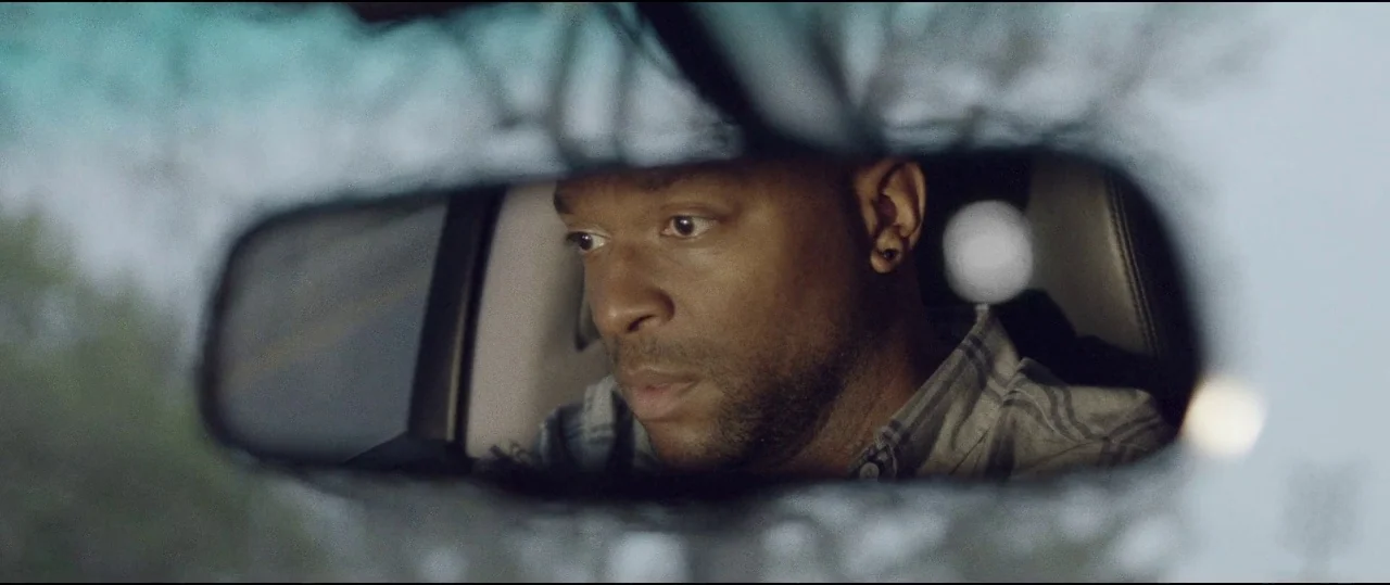 Lowlife (2017) movie still: closeup — A man is seated in the driver's seat of a car. The image is captured through the reflection of the rearview…