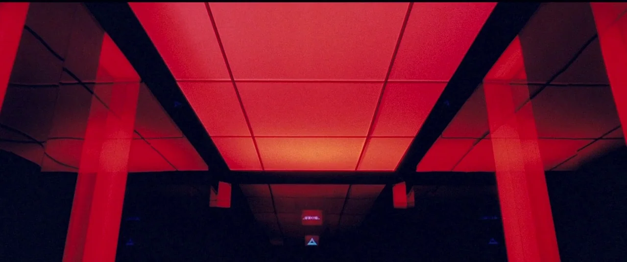 Beyond The Black Rainbow (2010) movie still: establishing — An empty corridor is illuminated by a series of glowing red ceiling panels. Parallel…