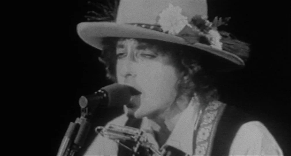 The Hurricane (1999) movie still: closeup — A man performs on a dark stage with a solid black backdrop. He sings into a microphone while positioned…