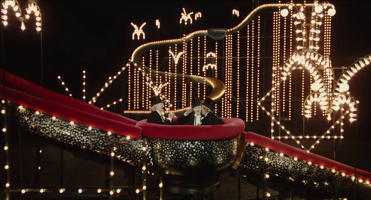 City of Women (1980) movie still: wide — A circular ride cart sits on a metallic track against a pitch-black background. Three men wearing tuxedos…