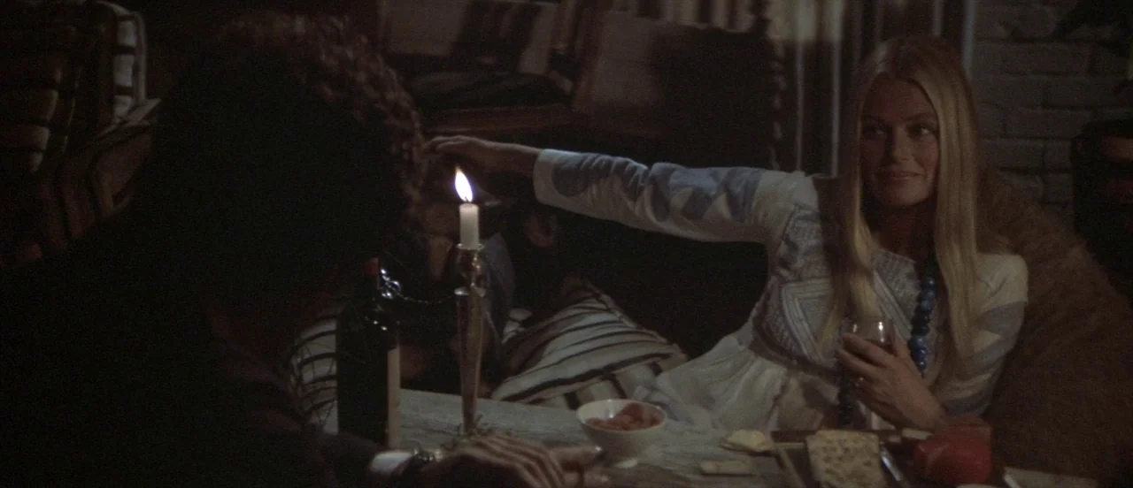 The Long Goodbye (1973) movie still: medium — A dimly lit setting features a table with a candle, a bowl, and food items. A woman smiles and reaches…