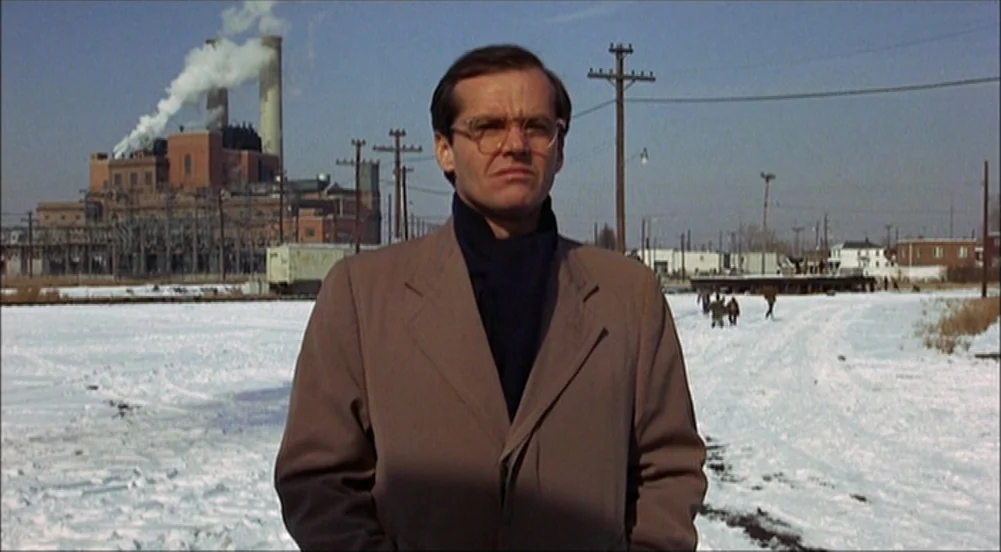 The King Of Marvin Gardens movie still: medium — An industrial site with snowy ground and a large brick factory in the background. A man stands in…