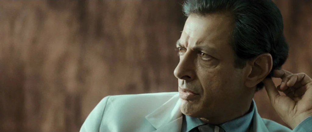Adam Resurrected (2008) movie still: closeup — A man stands in an indoor space against a textured, indistinct dark brown background. He rests his…